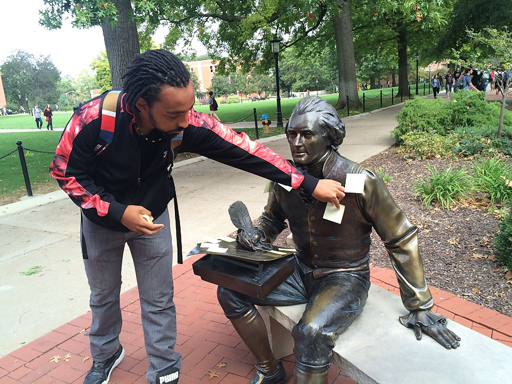 Senior Bryant Hill places sticky notes on the statue of Thomas Jefferson
